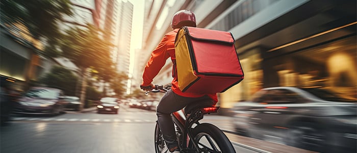 a food delivery cyclist rides a bike, carrying a red and yellow delivery box on his back
